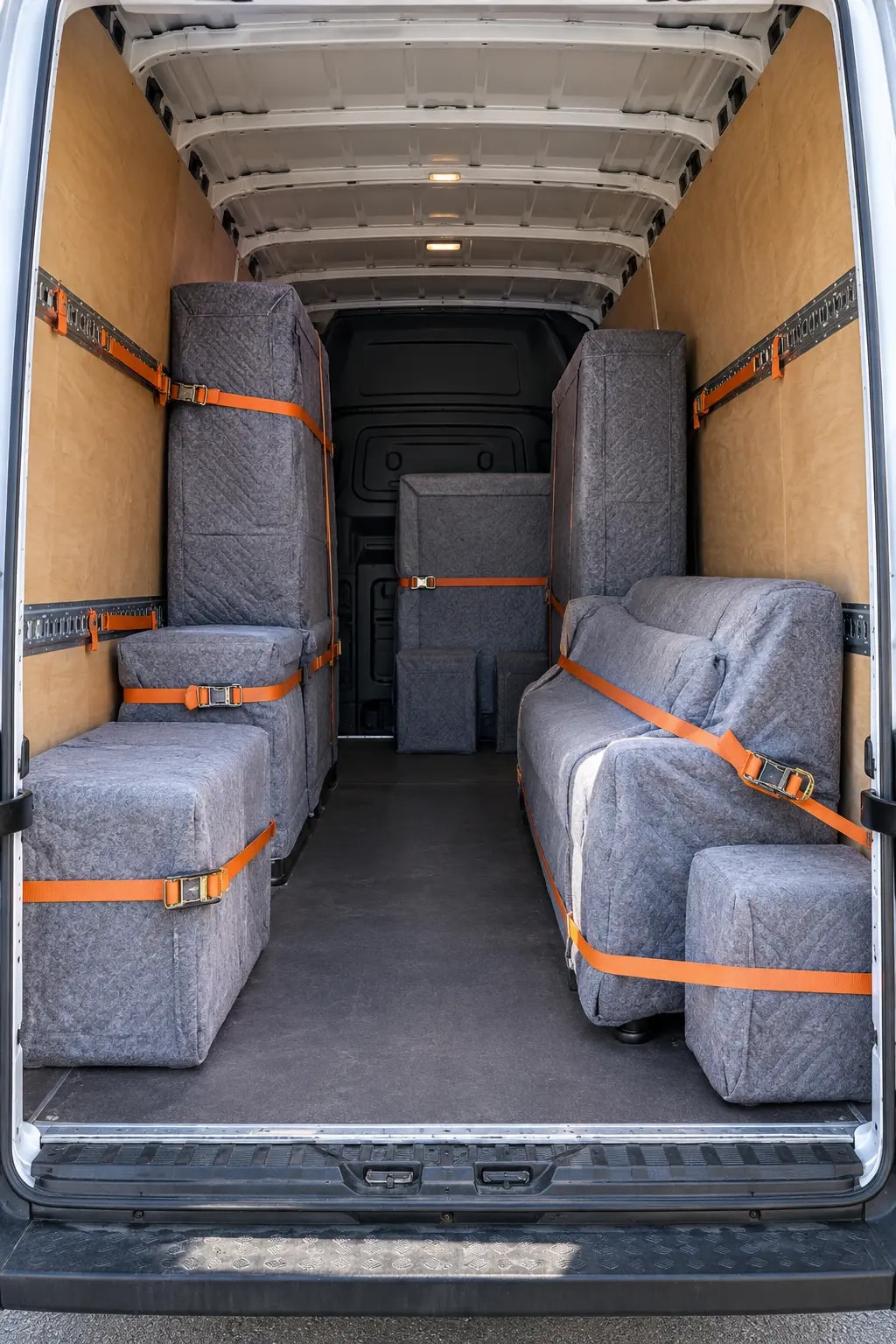 Blanket-wrapped furniture held in place by straps inside a removals van